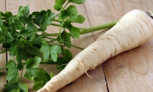 image of cream-colored, tapered parsley root next to parsley leaves on a pale wooden table